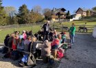 Walter Jonas spricht im Freien zu einer sitzenden Kindergruppe auf dem Bauernhof, daneben steht Heidi Ziegaus.