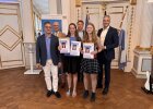 Zwei Schülerinnen des Von-Müller-Gymnasiums präsentieren ihre Urkunden, umgeben von Vertretern der Schule, der Regierung und weiteren Ehrengästen.