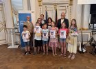 Mehrere Grundschulkinder halten Urkunden und Preisumschläge; eine Schülerin zeigt zusätzlich ein farbig gestaltetes Kunstwerk.
