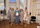 Eine Preisträgerin hält ihre Urkunde und steht mit Vertreterinnen und Vertretern von Regierung und Schule im Spiegelsaal.
