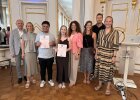 Zwei Preisträger halten Urkunden und stehen mit Vertreterinnen und Vertretern von Regierung und Schule im Spiegelsaal.