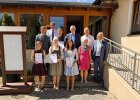 Eine kleinere Gruppe von Absolventinnen und Absolventen mit Urkunden steht gemeinsam mit Ehrengästen vor dem Veranstaltungsgebäude.