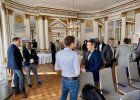 Mehrere Personen stehen im Spiegelsaal der Regierung der Oberpfalz in kleinen Gruppen zusammen und sprechen miteinander. Im Hintergrund sind Informationsaufsteller, Stehtische und Stuhlreihen zu sehen.